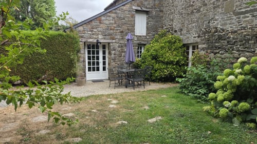 Stone cottage garden at Manoir de la Bégaudière with patio seating, hydrangeas, and manicured hedges in Mont-Dol