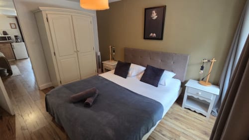 Spacious bedroom at Manoir de la Bégaudière in Mont-Dol with gray upholstered bed, white nightstand, and garden view