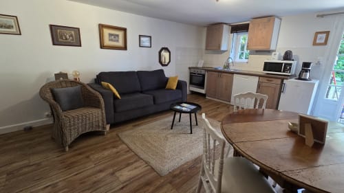 Spacious open-plan apartment at Manoir de la Bégaudière with dining table, dark sofa, wicker chair, and equipped kitchen in