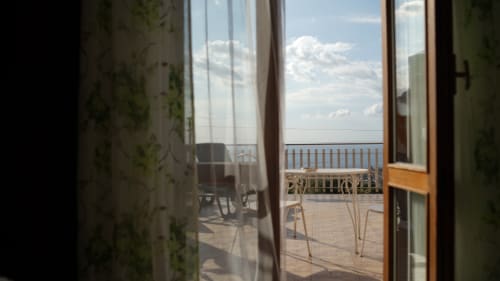 Porte in vetro aperte sulla terrazza fronte mare con sedie affacciate sul Mar Ionio, presso Pupi Catania Etna Farm B&B ad Aci