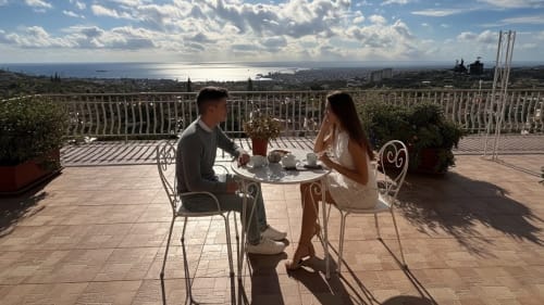 Coppia che cena in terrazza a Pupi Catania con vista mare su Aci Castello, Sicilia