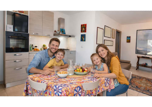 Famiglia di quattro persone che gustano un pasto al tavolo rotondo nella luminosa cucina del cottage della famiglia Sciara presso la Pupi Catania Etna Farm B&B, Aci