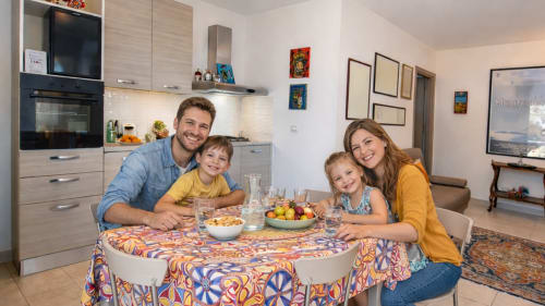 Famiglia sorridente intorno al tavolo nella cucina moderna della casa di vacanza Pupi Catania Etna Farm B&B ad Aci Castello, Sicilia
