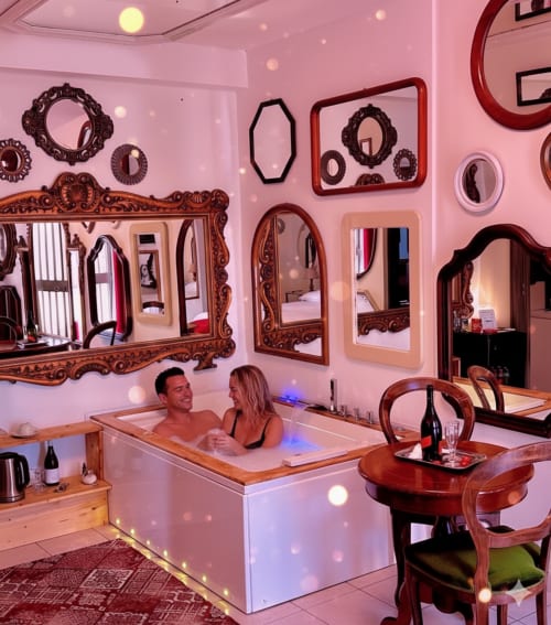 Coppia che si rilassa nella vasca idromassaggio con luci rosa, specchi decorativi e arredamento in legno della Pupi Catania B&B, Aci