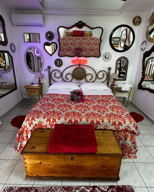 Camera da letto lussuosa al Pupi Catania B&B con biancheria rossa decorata, testata in ferro battuto ornamentale e specchi decorativi