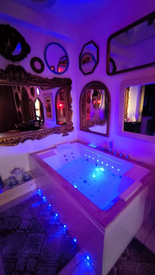 Lussuoso bagno con idromassaggio, illuminazione ambientale viola, vasca jacuzzi illuminata e specchi ornati presso il Pupi Catania B&B