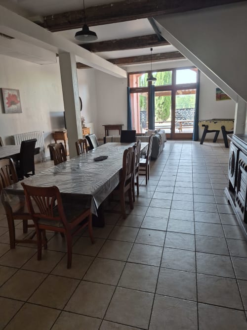 Spacious dining room at Domaine De Poulharies with wooden beams, large table, and glass doors overlooking Carcassonne