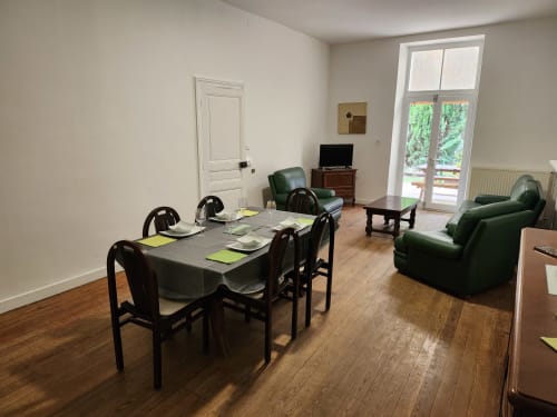Salle à manger du gîte Blanquette au Domaine De Poulharies à Carcassonne, avec table, fauteuils verts, télévision et terrasse