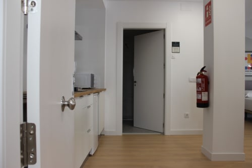 Pasillo moderno del estudio Palacio Mambrilla en Valladolid, con puertas blancas, suelo de madera y extintor.