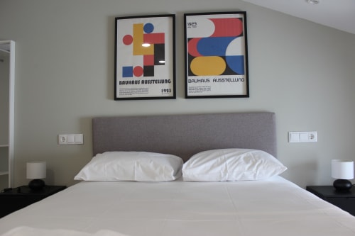 Habitación de estudio moderna en Palacio Mambrilla de Valladolid con cabecero tapizado gris, ropa de cama blanca y estilo Bauhaus