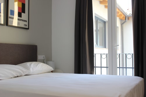 Moderna habitación en el hotel Palacio Mambrilla de Valladolid con ropa de cama blanca, cabecero marrón y puertas al balcón con vista a la ciudad
