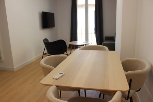 Área de comedor moderno con mesa de madera y sillas beige en apartamento de Valladolid, televisor y vista de la ciudad visible