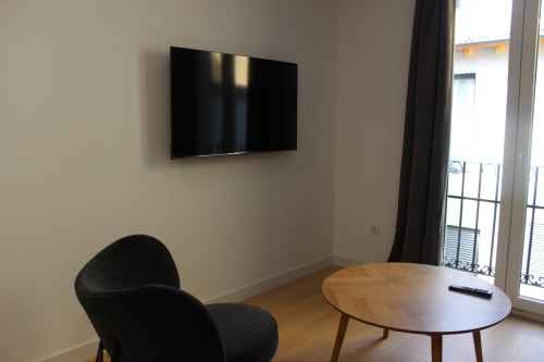 Moderno estudio en Valladolid con TV de pared, mesa de madera, silla negra y acceso a balcón