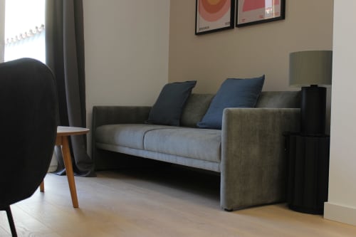 Sala de estar moderna con sofá gris, cojines azules, silla de madera y lámpara en apartamento Palacio Mambrilla, Valladolid