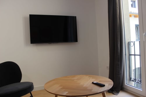 Sala de estar moderna en Palacio Mambrilla con televisor montado en pared, mesa redonda de madera y vistas a la ciudad