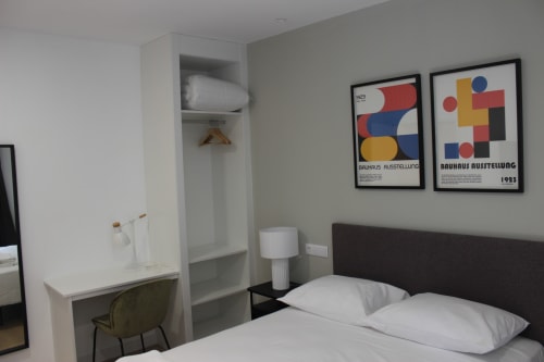 Dormitorio moderno en Palacio Mambrilla, Valladolid con ropa de cama blanca, cabecero oscuro, pósters Bauhaus y zona de trabajo.