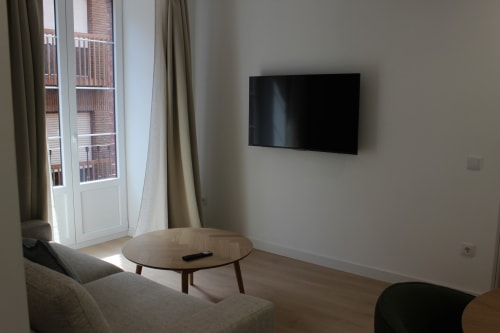 Moderna sala de estar del apartamento Palacio Mambrilla Valladolid con TV empotrada, mesa de madera y vista al balcón de ladrillo rojo