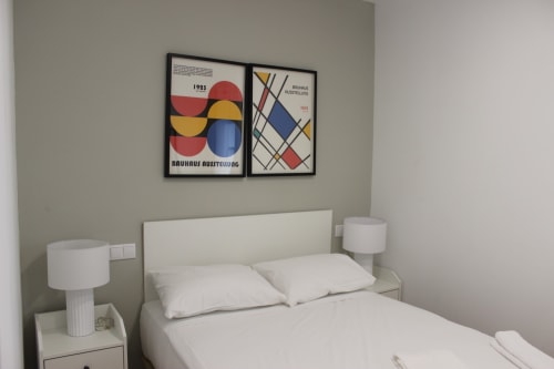 Moderno dormitorio en Palacio Mambrilla de Valladolid con cama blanca, mesillas y arte Bauhaus sobre el cabecero