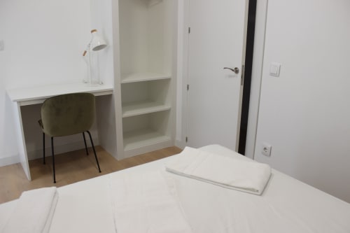 Moderno dormitorio con escritorio, silla, estanterías y ropa de cama blanca en el apartamento Palacio Mambrilla de Valladolid