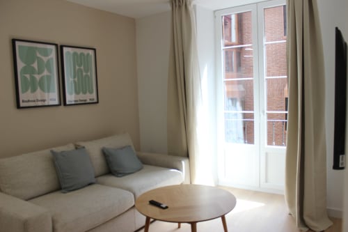 Moderna sala de estar en Palacio Mambrilla Valladolid con sofá beige, mesa redonda y balcón con vistas a la ciudad