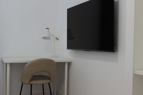 Escritorio con silla tapizada y lámpara bajo TV en pared del apartamento Palacio Mambrilla, Valladolid
