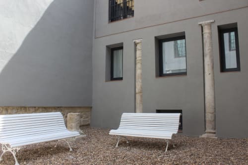 Dos bancos blancos en el patio del estudio Palacio Mambrilla, Valladolid, con fachada y ventanas modernas