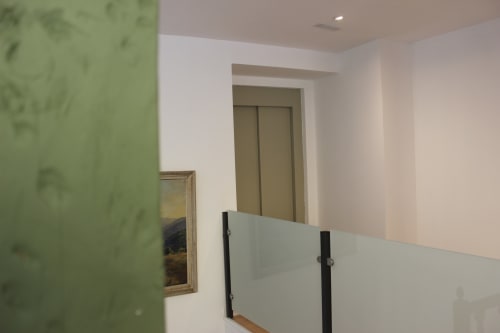 Pasillo moderno con pared de acento verde, barandillas blancas y puertas de ascensor en el apartamento Palacio Mambrilla de Valladolid