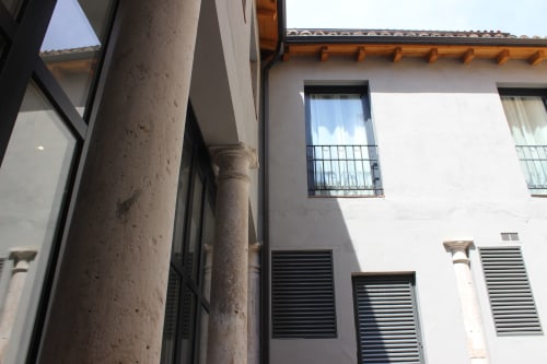 Patio del Palacio Mambrilla en Valladolid: columna de piedra, fachada blanca con balcones y contraventanas de madera