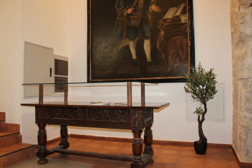 Mesa de exhibición de madera ornamentada con tapa de cristal en apartamento Palacio Mambrilla, Valladolid, con pintura clásica encima