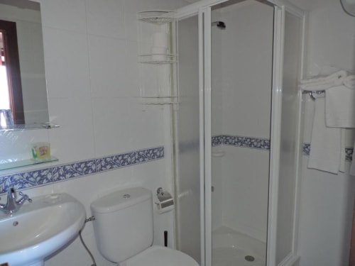 Baño moderno en estudio de Casa Rural Los Helechos con azulejos blancos, cenefa decorativa azul, lavabo, inodoro y ducha de esquina