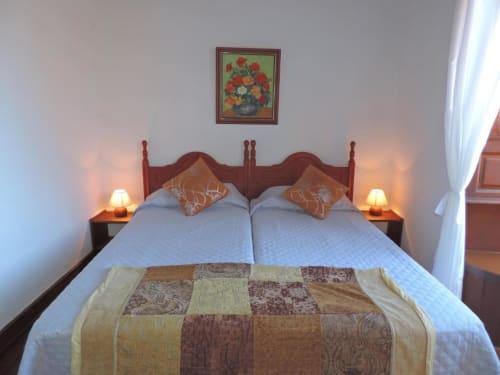 Acogedor dormitorio de estudio en Casa Rural Los Helechos con cama de madera, ropa de cama azul, cojines decorativos, lámparas de noche y detalles florales