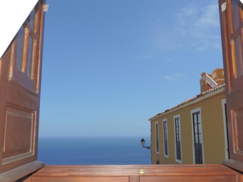 Puertas de madera abiertas al mar en Casa Rural Los Helechos en Agulo, con edificio amarillo y horizonte azul oceánico
