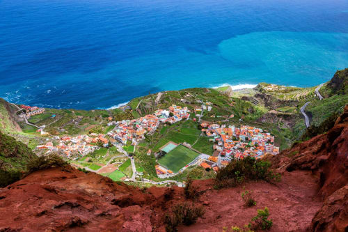 Vista aérea de Agulo con acantilados volcánicos rojos, tejados de barro y cala turquesa en Canarias