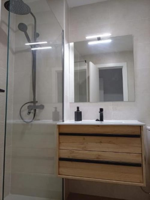 Baño moderno con tocador de madera, espejo grande y ducha tipo suite en Apartamentos La Machacona, Cáceres