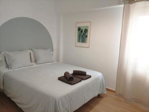 Dormitorio luminoso en Apartamentos La Machacona en Cáceres con cabecera arqueada, ropa de cama blanca y obra de arte verde en la pared
