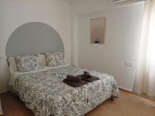Dormitorio moderno en apartamento de Cáceres con cabecero arqueado, ropa de cama estampada y suelo de madera