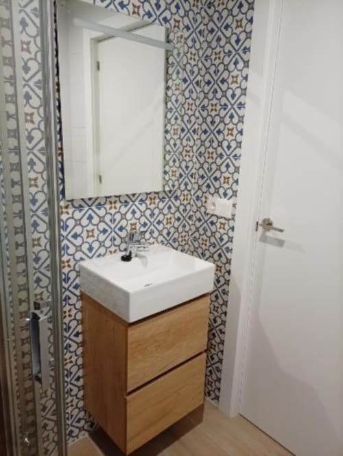 Moderno lavamanos de baño con lavabo blanco, mueble de madera y azulejos de patrón azul en apartamento de Cáceres