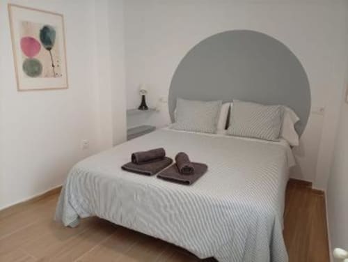 Dormitorio moderno en Apartamentos La Machacona en Cáceres con cabecera circular gris, ropa de cama blanca, suelo de madera y