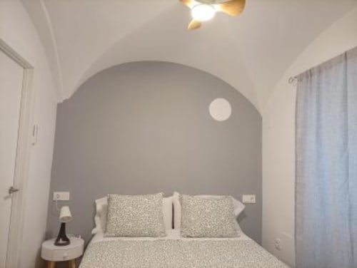 Dormitorio moderno con pared de acento arqueada gris, ropa de cama blanca e iluminación colgante en Apartamentos La Machacona, Cáceres