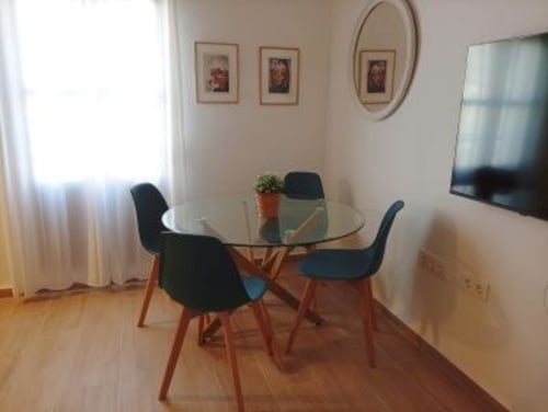 Comedor moderno en apartamento de Cáceres con mesa redonda de cristal, sillas negras, pisos de madera y vistas a la ciudad