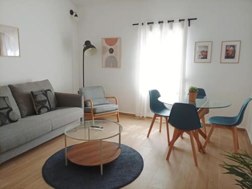 Luminoso salón moderno en apartamento de Cáceres con sofá gris, mesa de comedor y vistas a la ciudad desde amplios ventanales