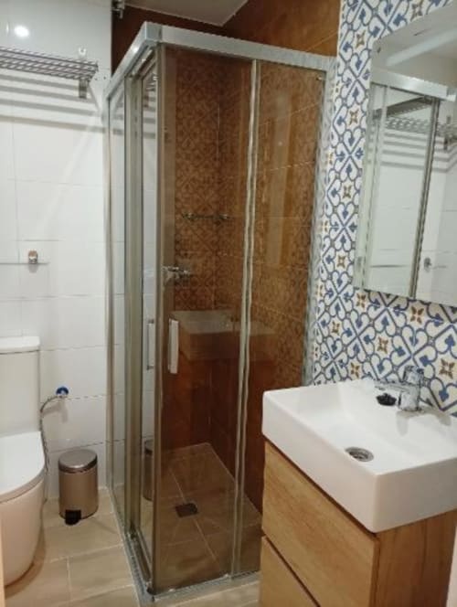 Baño moderno con ducha a ras de suelo, lavabo blanco y detalles decorativos de azulejos azules y blancos en apartamento de Cáceres