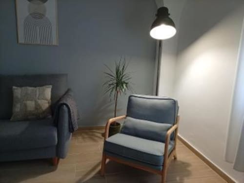 Salón moderno en apartamento de Cáceres con sillón azul, sofá, lámpara colgante, planta y suelos de madera