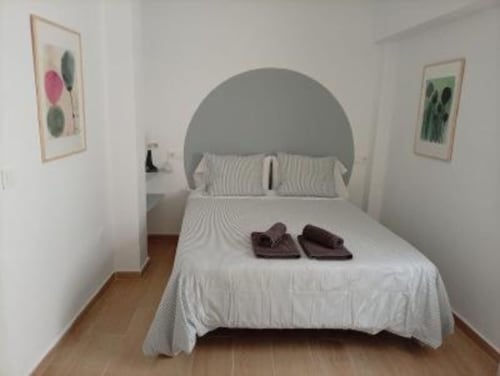 Dormitorio moderno con cabecero circular gris, ropa de cama blanca y almohadas a rayas en Apartamentos La Machacona, Cáceres