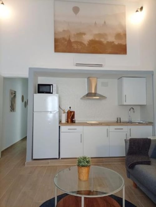 Cocina y sala de estar modernas en apartamento de Cáceres con muebles blancos, electrodomésticos de acero inoxidable y vista al monumento
