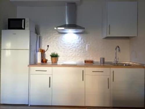 Cocina moderna en apartamento de Cáceres con gabinetes blancos, encimera de madera, electrodomésticos de acero inoxidable y campana extractora