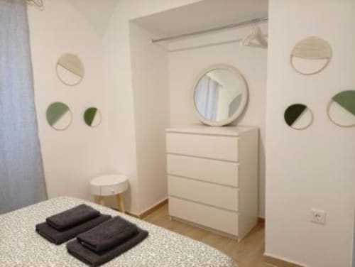 Dormitorio moderno en Apartamentos La Machacona, Cáceres, con cómoda blanca, espejos circulares y cojines negros en la cama