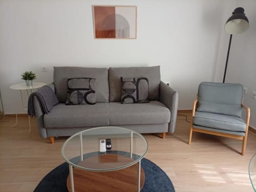Sala moderna de apartamento en Cáceres con sofá gris, butaca, mesa de cristal redonda y arte geométrico en pared