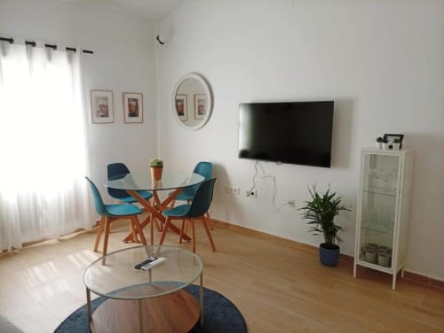 Sala de estar moderna con comedor, sillas azules, televisor de pantalla plana y decoración blanca en edificio histórico de Cáceres