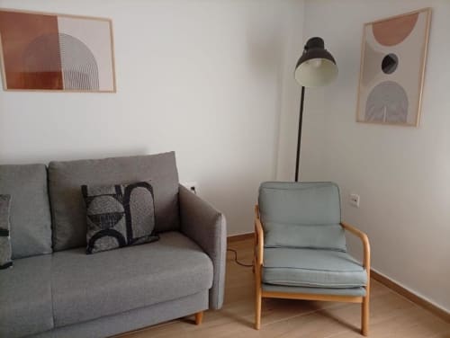 Moderno salón en el apartamento La Machacona de Cáceres con sofá gris, sillón, lámpara de pie y arte abstracto en la pared.